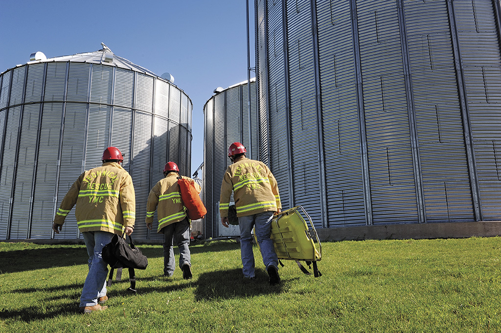 Three firefighters wearing PPE walking toward grain bins holding grain bin rescue equipment