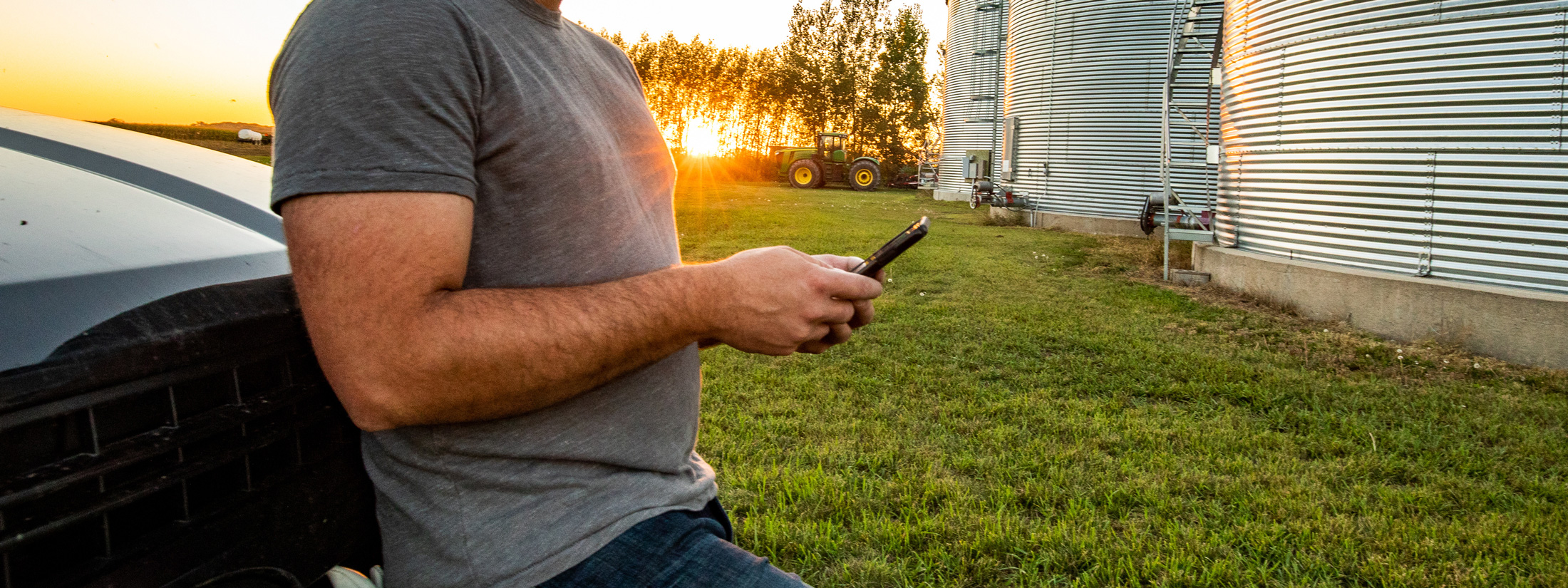 Man holding cell phone with grain bins in background